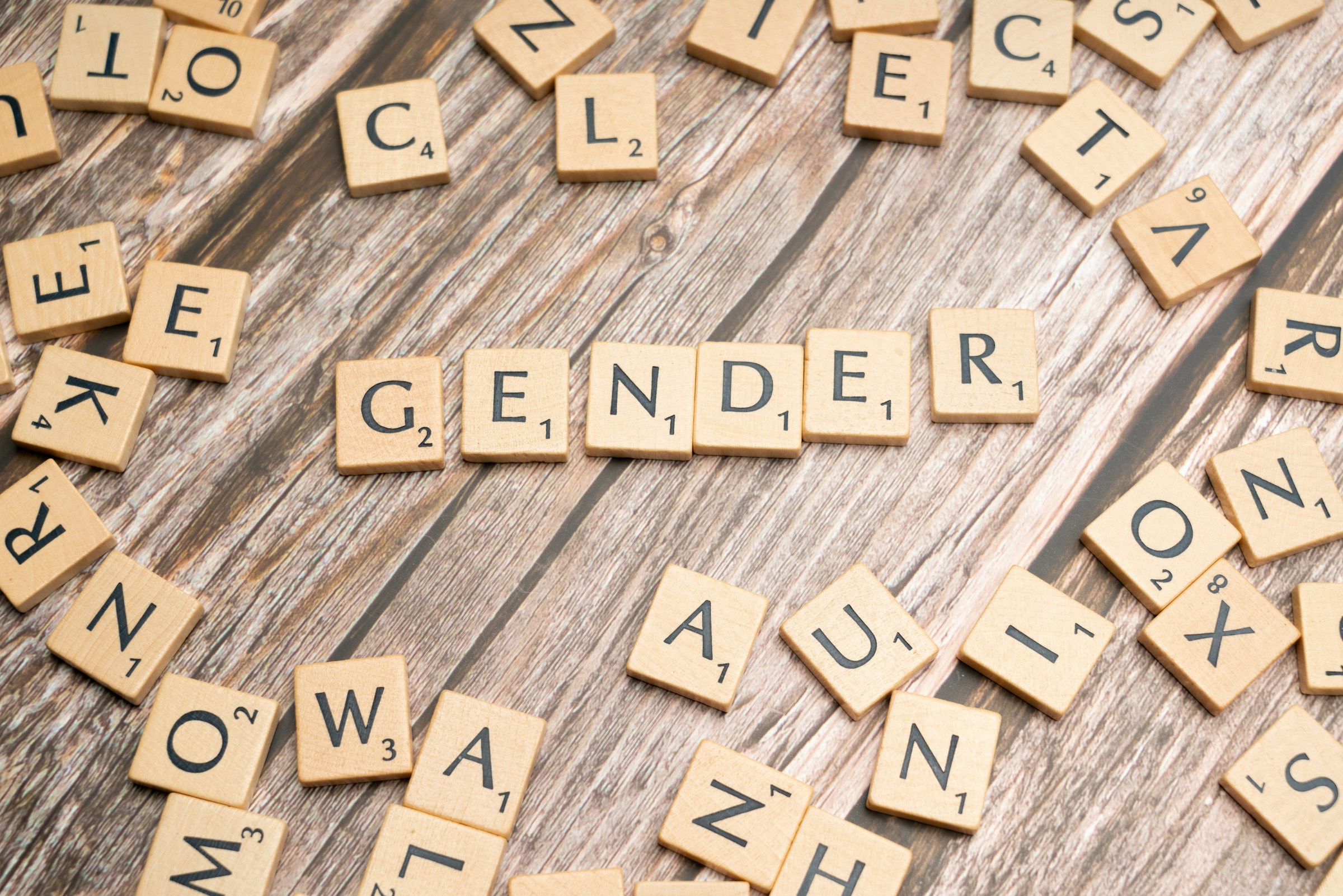 Wooden scrabble tiles spelling the word "gender" on a wooden table